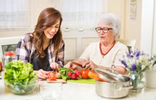 caregiver and an elderly woman trying to prepare meal